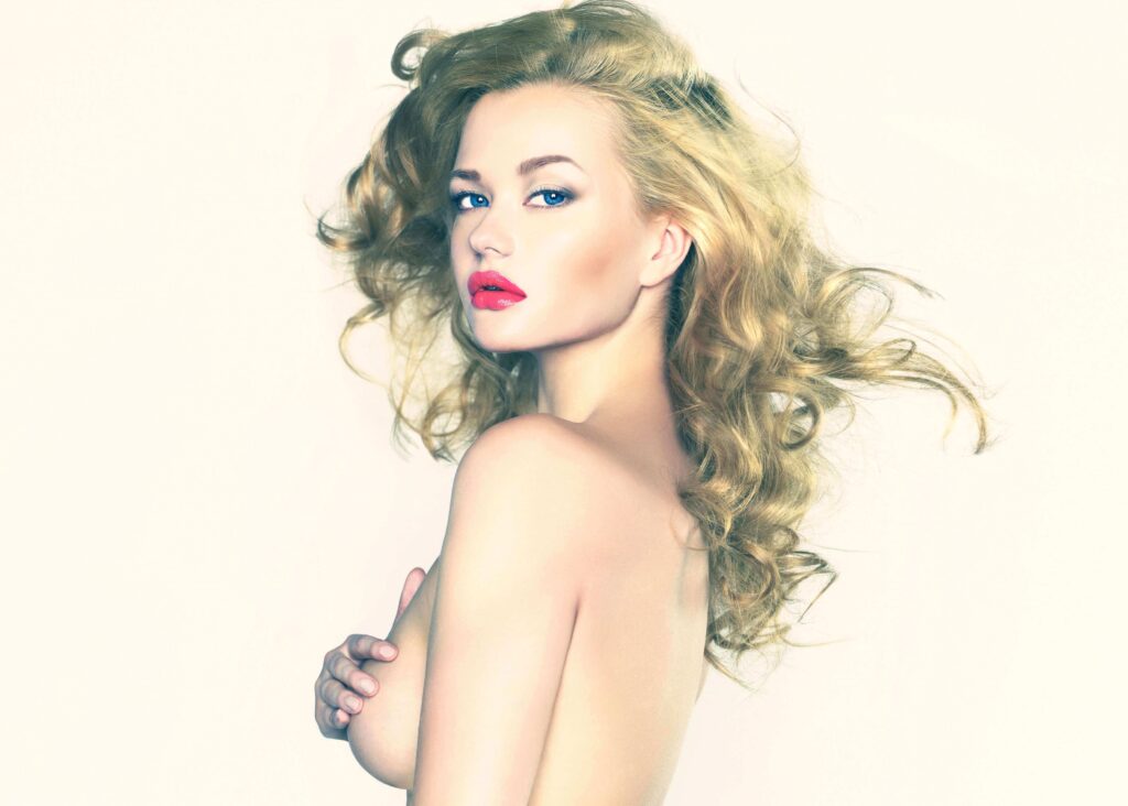 Dramatic portrait of young woman, standing at an angle, naked, with a hand up to cover her visible breast