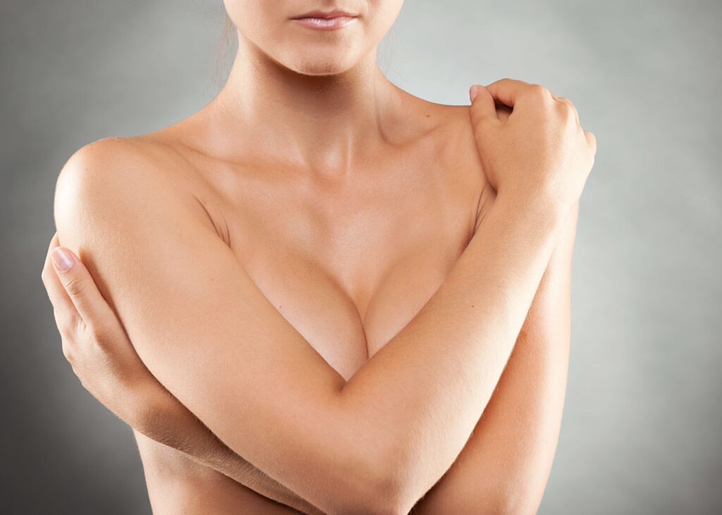 Naked woman protectively folding arms over breasts