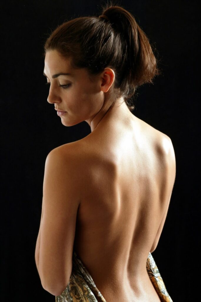 Young woman showing her back, holding a sheet draped elegantly over her front