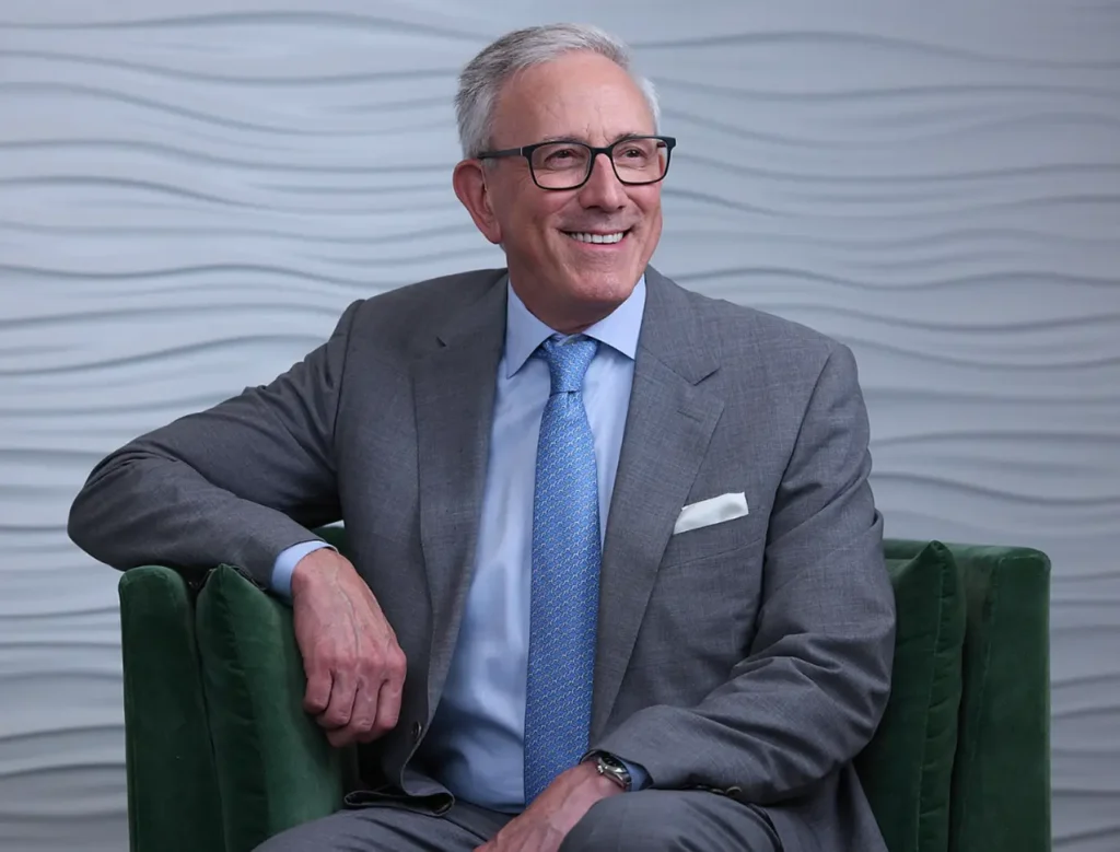 Dr Romanelli is seated casually on a modern green armchair, smiling