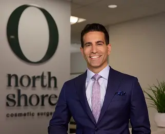 Dr. John Layliev standing in front of logo signage in the office, smiling