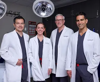 The full team of doctors, in their white coats, standing together smiling in an operating room